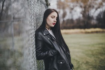 woman leaning on cyclone fence with her right hand on her right jacket pocket