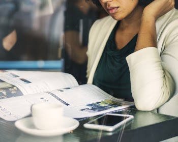 Woman Leaning on Desk Reading Newspaper