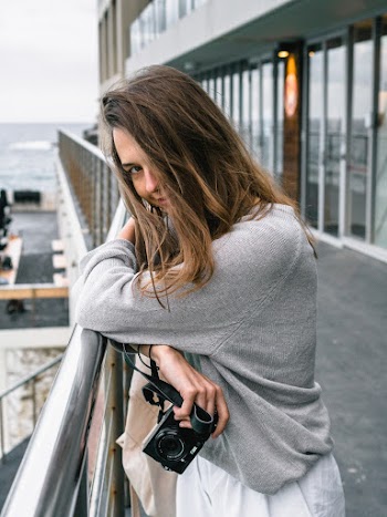 Woman Leaning On Grey Metal Fence Holding Black Camera