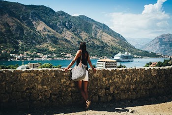 Woman Leaning on Rock Wall Near Body of Water and Mountain