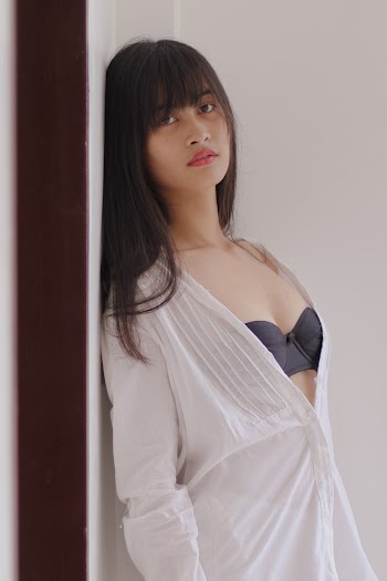 Woman Leaning on Wall Wearing Sheer White Top And Black Brassiere