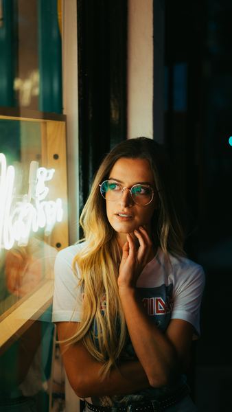 woman leaning on white wall with eyeglasses taking photo inside dark room