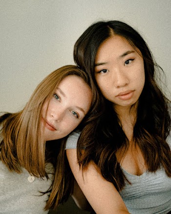 Woman Leaning on Woman's Shoulder Wearing Gray Top