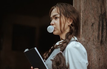 Woman Leaning on Wood Wall While Blowing Bubble Gum