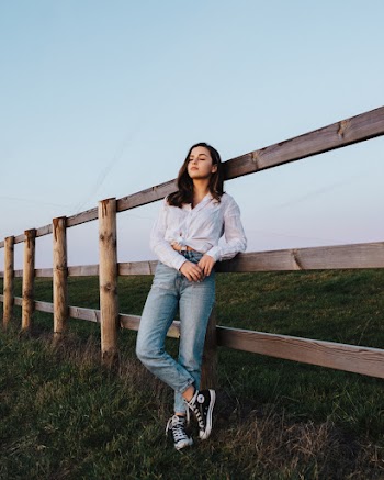 Woman Leaning on Wooden Fence While Standing on Grass Field