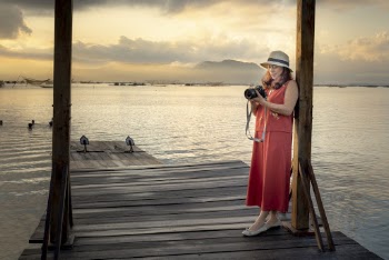 Woman Leaning on Wooden Post Holding a Camera