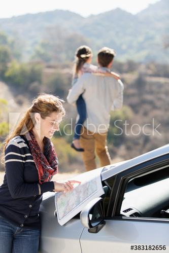 Woman looking at map on car at sunny roadside