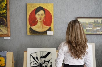 Woman Looking At Paintings Displayed On The Wall