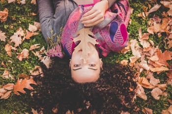 Woman Lying Down On Green Grass Field Holding Brown Leaf