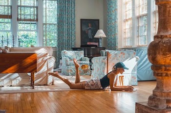 woman lying on brown floor near blue and white sofa set inside white room with glass windows at daytime
