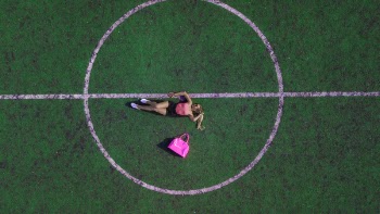 Woman Lying on Field Beside Pink Bag