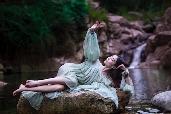 woman lying on large stone between flowing river