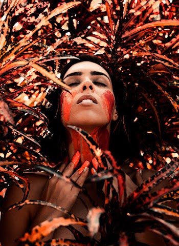 Woman Lying on Orange-and-black Plants With Orange Paint on Neck and Face