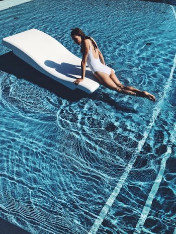 woman lying on white lounge chair in the middle of pool