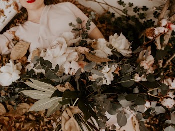 Woman Lying on White Surface With Plants and Flowers