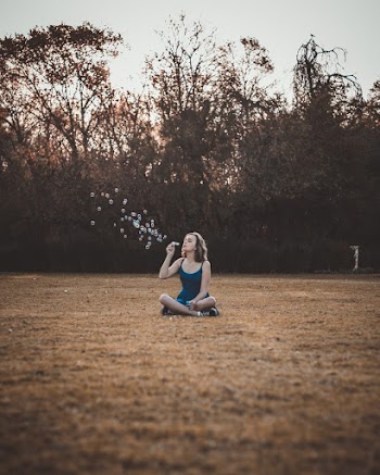 Woman Making Bubbles Sitting On Grass Field