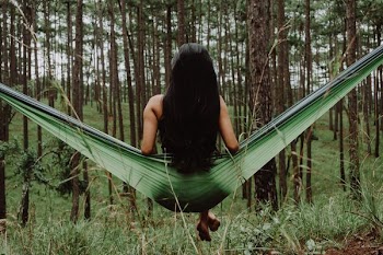 woman on green hammock swing facing trees