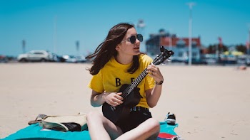 Woman Playing Ukulele While Sitting on Blue Textile