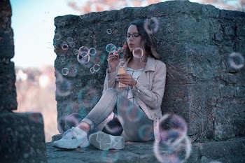 woman playing with bubbles while leaning on concrete wall