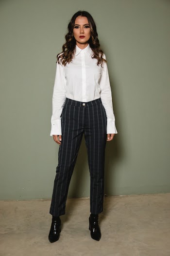 Woman Posing in White Dress Shirt and Black Pants Standing Against Gray Wall 