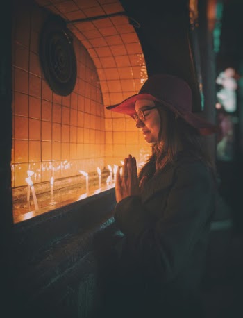 Woman Praying In Front of Lit Candles