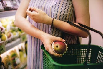 Woman Putting Red Apple on Green Shopping Basket