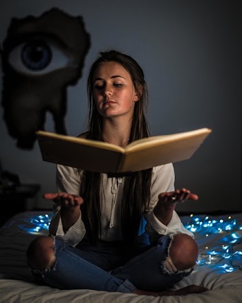 Woman Reading a Book Sitting on Mattress Near the Blue String Light Inside the Room