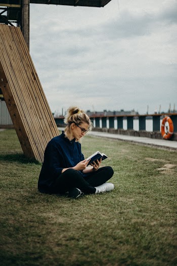 Woman Reading a Book While Sitting in Grass Field
