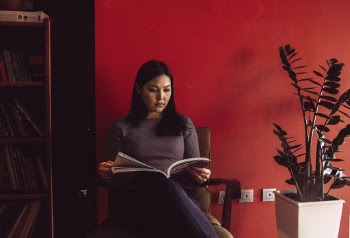 Woman Reading Beside Red Painted Wall
