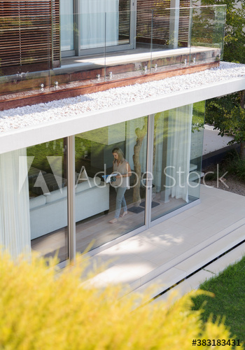 Woman reading book at window of luxury modern house