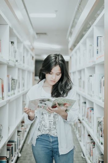woman reading book on pathway between book shelf