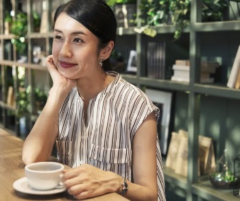 Woman Seated Near a Shelf Holding Coffee Cup