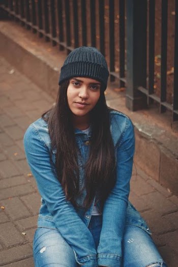 woman sits on gray concrete pavement near black metal fence