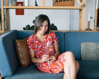 Woman Sitting at Sofa Wearing Red and Multicolored Floral Dress White Holding Glass