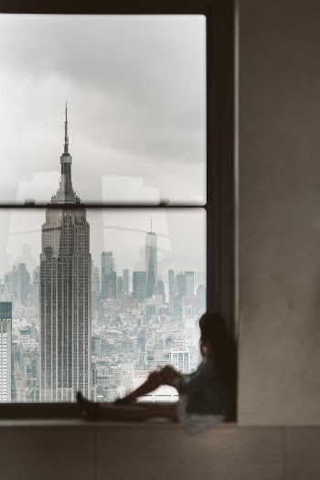 Woman Sitting at Window Sill Looking Out the Window at New York City