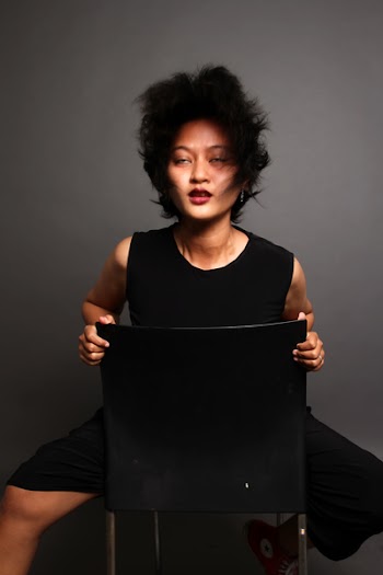 Woman Sitting Backward on Black Chair With Gray Background