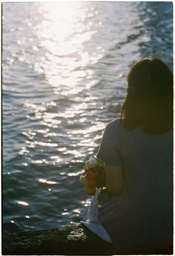 Woman Sitting by the Water and Holding a Bunch of Flowers