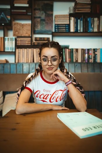 woman sitting inside library while leaning hands on brown wooden table