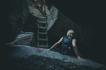 woman sitting of gray rock beside wooden ladder