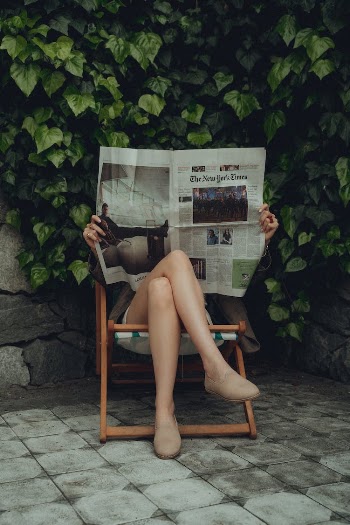 Woman Sitting on a Lounge Chair and Reading a Newspaper