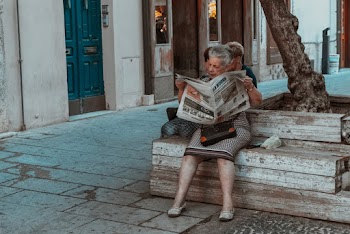 Woman Sitting on a Wooden Bench Reading a Newspaper