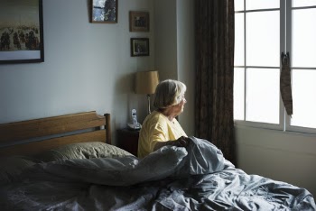 Woman Sitting On Bed Looking Out Window Inside Room