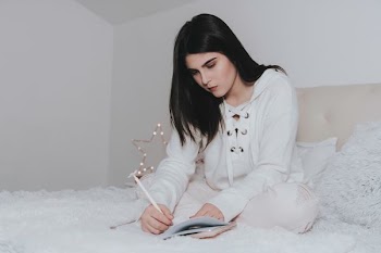 woman sitting on bed while writing on notebook