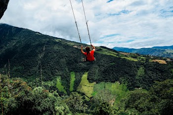 Woman Sitting on Big Outdoor Swing Viewing Mountain Under Blue and White Skies