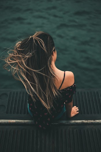 Woman Sitting On Black Surface Overlooking Body Of Water