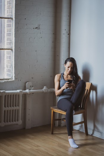 Woman Sitting on Brown Wooden Chair Near Window While Using Smartphone
