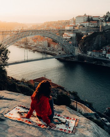 Woman Sitting on Cliff Overlooking Bridge