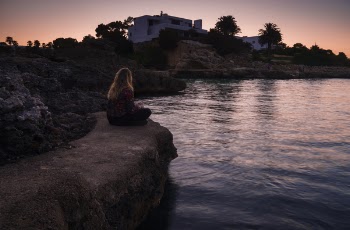 Woman Sitting on Edge of Rock Near Body of Water