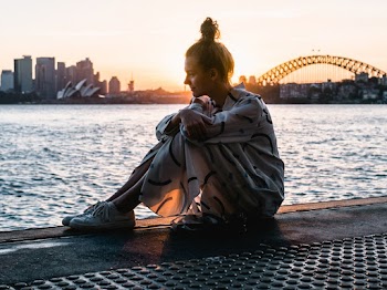 Woman Sitting on Floor Near Body of Water