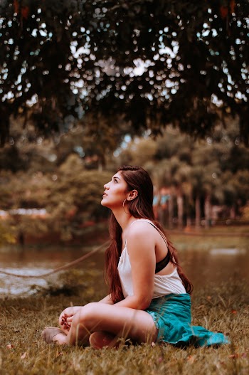 Woman Sitting on Grass Looking Upwards Near Tree